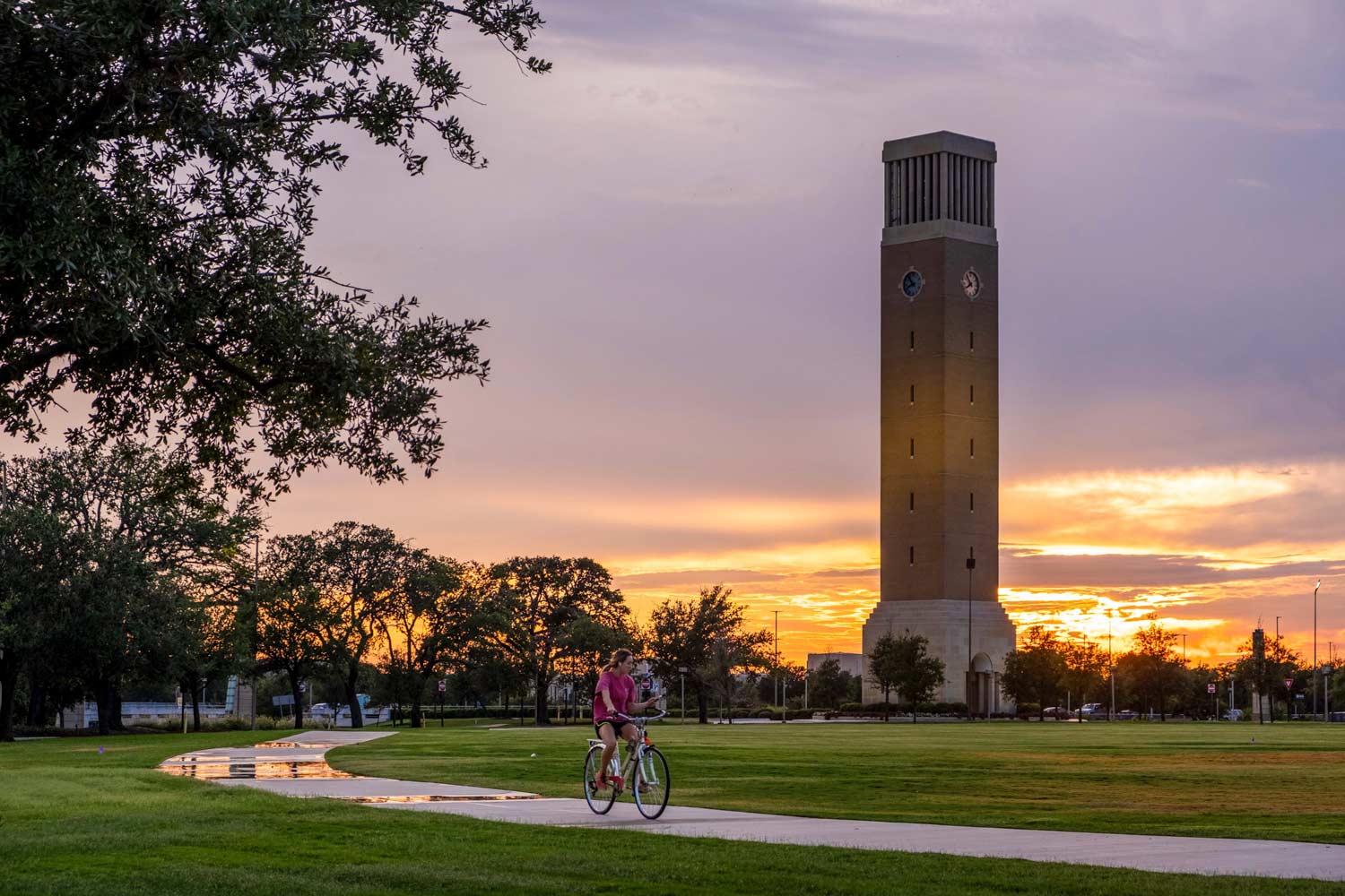 91Ƶ student rides a bike in front of Albritton Bell Tower during sunset.